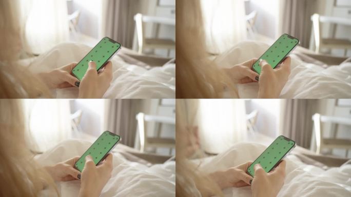 有绿屏模型和跟踪标记的智能手机，一个女人坐在白色的床上刷着社交媒体。