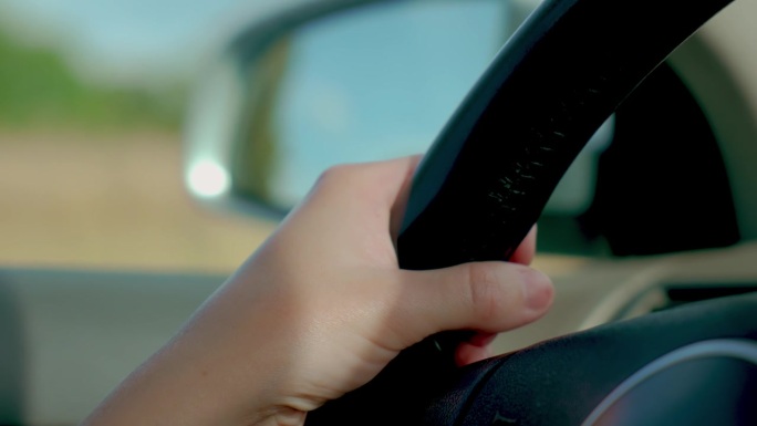 近距离拍摄的女性手握方向盘，她驾驶的汽车外镜反射
