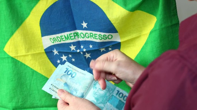 这名妇女在巴西国旗的背景下数巴西雷亚尔的钱，金融经济概念，100雷亚尔后的纸币档案