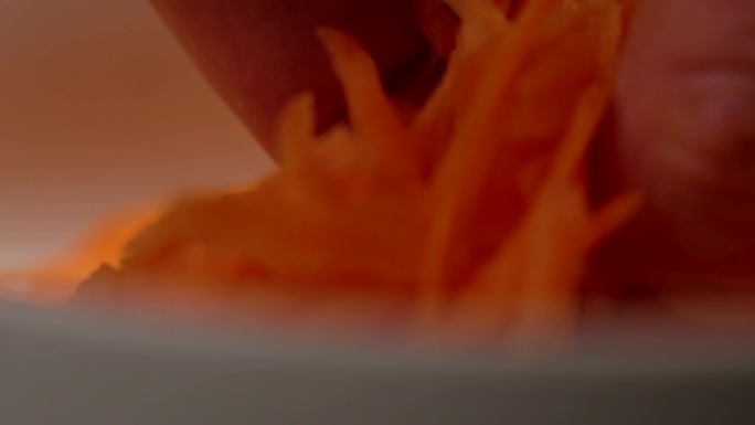 厨师手拿生磨碎的胡萝卜丝。切碎的蔬菜特写