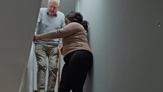 老人、男子或照顾者在安宁疗护或住家用拐杖扶楼梯、协助或指引。老年人，男性或女性和沟通，步骤或残疾在退