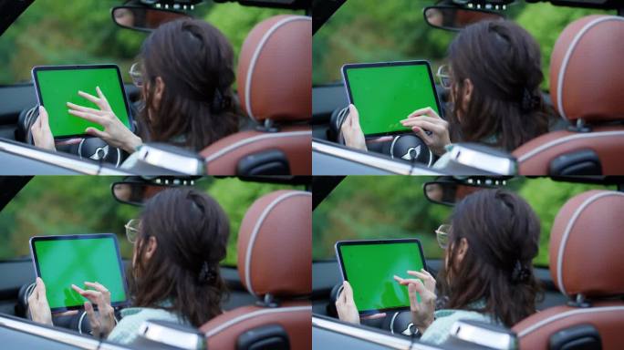 坐在车里滚动绿屏平板电脑的女人。女司机在车内使用色度键装置。从肩膀上看。