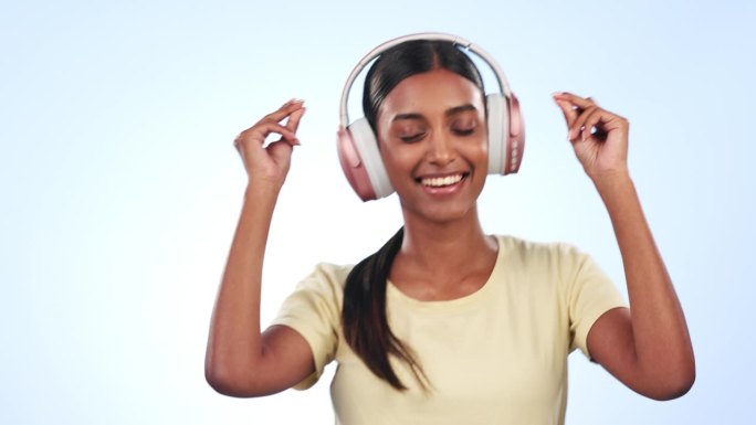 快乐的女人，戴着耳机，伴着音乐、播客或歌曲在录音室的背景下跳舞。女性微笑着听着耳机，享受着音频流、音