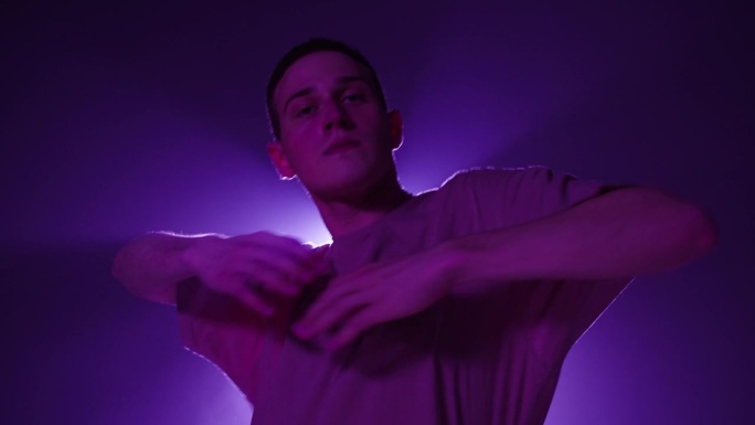 年轻人在工作室里用紫色的光在黑暗的背景上跳着现代舞。现代慢舞编舞的拍摄。男舞蹈编导在舞蹈动作中表达感