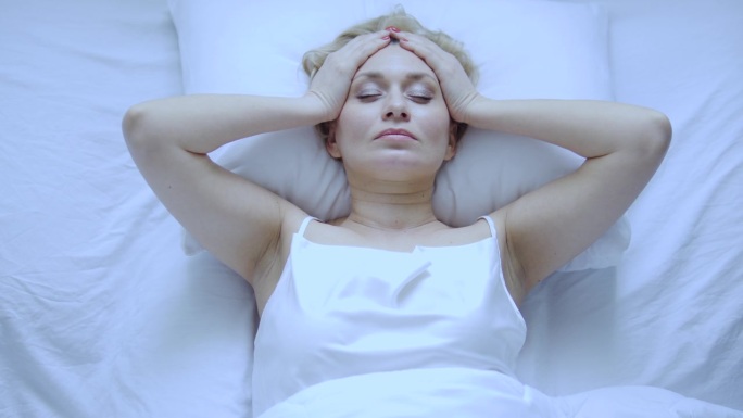 不安分的女人躺在床上头痛，按摩头部，患有血压问题，开始更年期或月经，俯视图