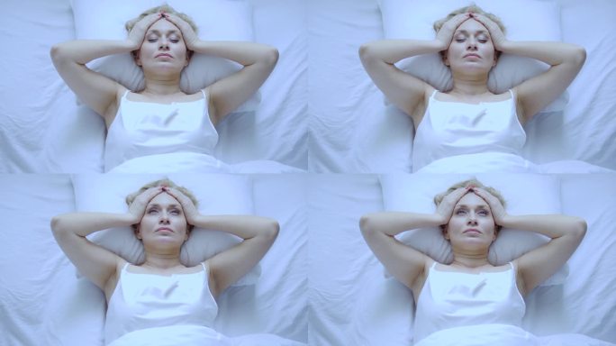 不安分的女人躺在床上头痛，按摩头部，患有血压问题，开始更年期或月经，俯视图