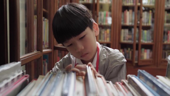 可爱又聪明的亚洲小学生在学校图书馆的木书架上找书