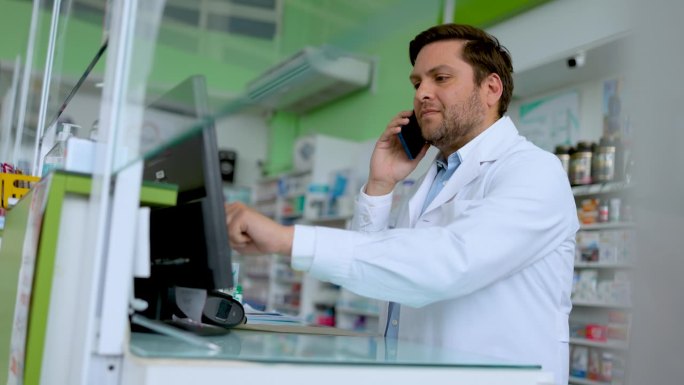 拉丁美洲的男药剂师一边在电话里接送货单，一边在电脑上查看是否有货