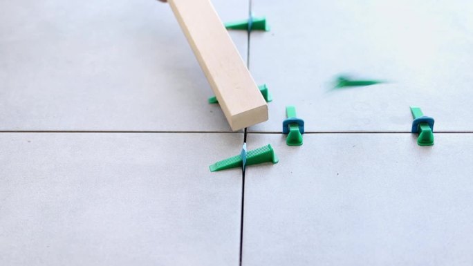 瓷砖在慢动作中将瓷砖调平系统的楔子从地板上敲下来。瓷砖找平系统采用塑料夹和楔子，在瓷砖砂浆套上的同时