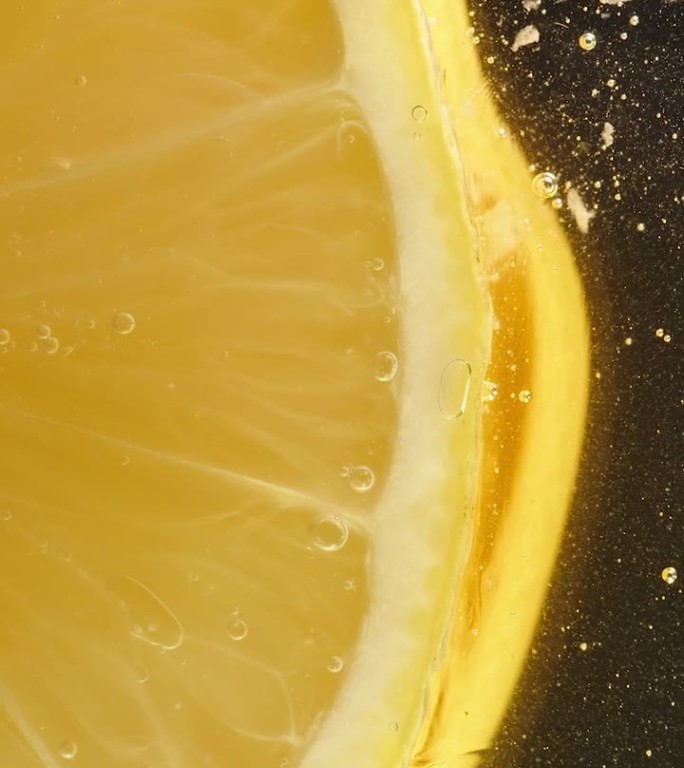 玻璃桌子上柠檬片的底部，蜂蜜滴下来，特写在黑色背景下。垂直视频。