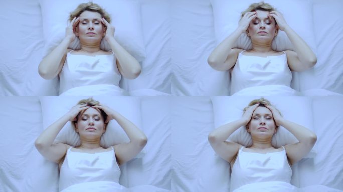 不开心的烦恼的女人躺在床上按摩头部，感觉不愉快的头痛，血压问题，偏头痛因为更年期开始