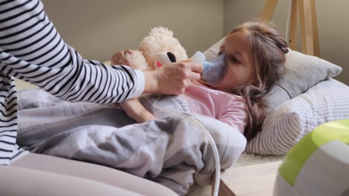小女孩用喷雾器吸气，可爱的妈妈给生病的孩子吸气，妈妈帮助感冒和流感的女儿吸入喷雾器气雾剂。