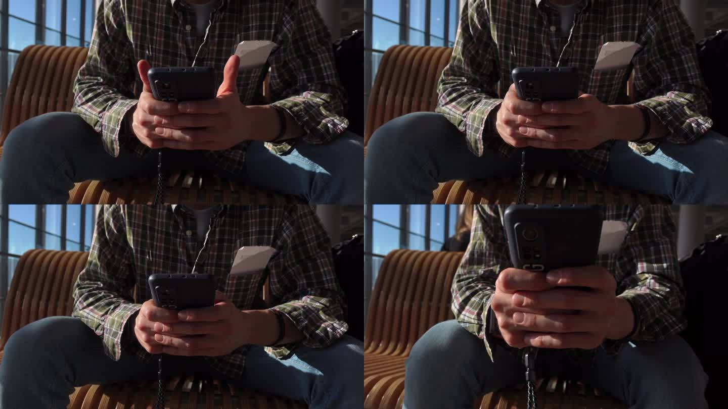 男性坐在机场候机时用智能手机发短信的特写