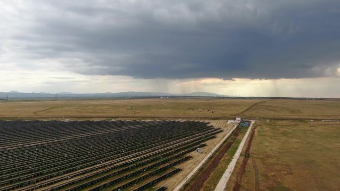 一个太阳能电池板农场的鸟瞰图，俯瞰着地平线上的山脉，上面悬挂着雷雨云。可再生能源。绿色能源。对环境的