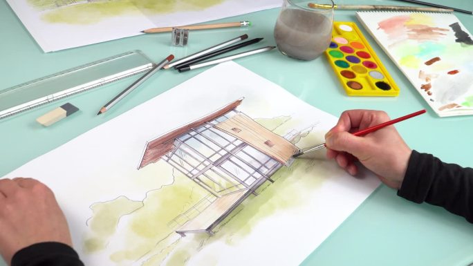插画家的手在使用水彩颜料和刷子的模块化预制房屋的手绘插图工作的镜头。