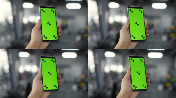 男子手持智能手机与chromakey在健身房，特写。男子手持绿色屏幕的智能手机，背景是健身房。概念技