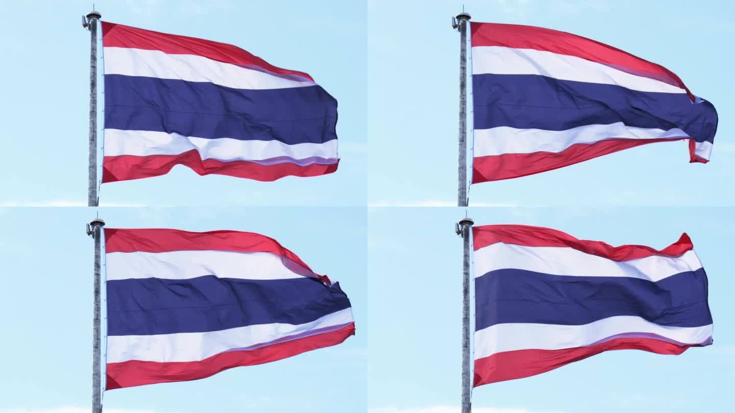 泰国国旗悬挂在白色的高钢杆上，被风吹起，在湛蓝的天空和白云的背景下形成了生动的波浪。