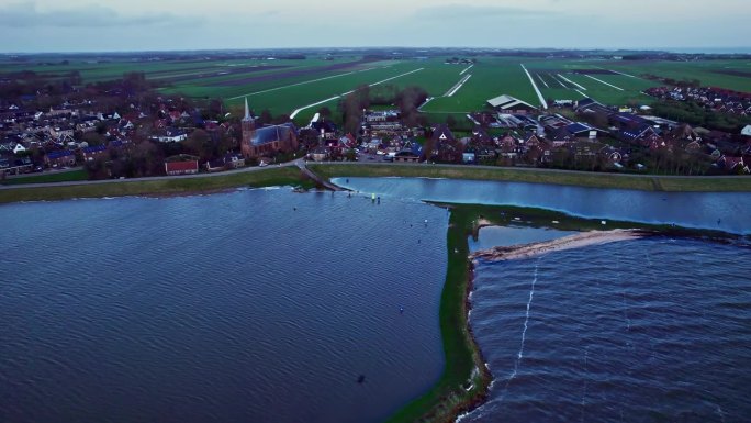 在蓝色的马克米尔湖的大堤后面，荷兰一个村庄被洪水淹没的海滩的空中轨道拍摄