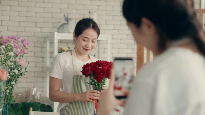 快乐的亚洲女花艺师合作制作花卉杰作，用智能手机捕捉社交媒体营销的快乐时刻…