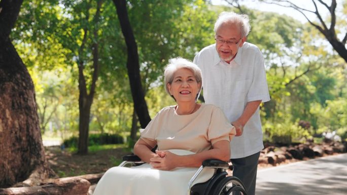 快乐的亚洲老人在公园外为妻子推轮椅，老年夫妇和退休生活的概念