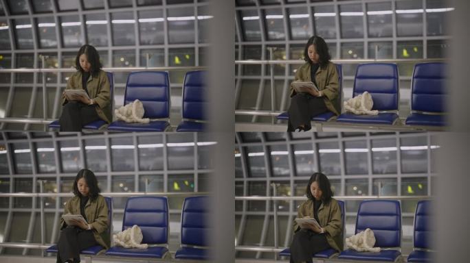一段4k视频显示，一名年轻女子晚上在机场候机大厅触摸和使用数码平板电脑。