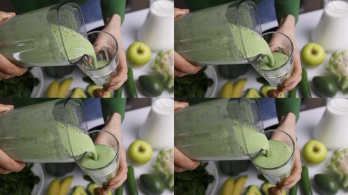 一名妇女将自制的新鲜绿色冰沙倒入玻璃杯中，这种冰沙由健康的蔬菜和水果制成。健康的生活方式