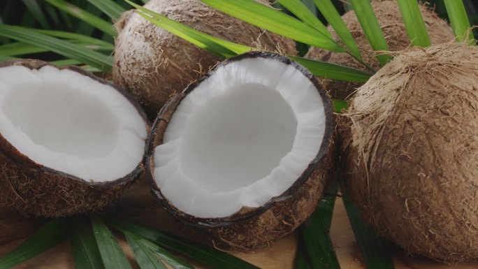 刚打开的椰子和椰子片、椰子叶在木桌上慢慢旋转。很好的水果背景为您的项目。将椰奶倒入其中一半的椰子中。