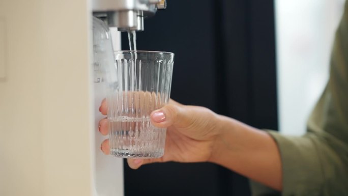 成熟女人用手从家里的滤水器中压水。