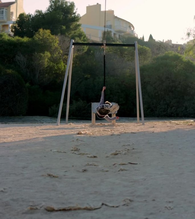 垂直视频一个活跃的男孩在树上自制的蹦极上荡秋千，或者在城市公园户外玩耍。