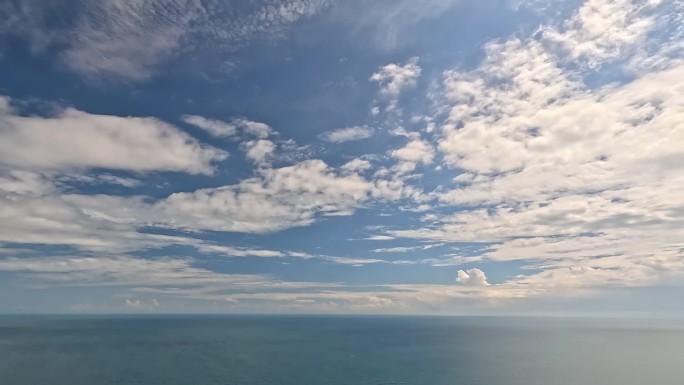 在平静的海面上，蓝色的夏日天空中飘动着飘忽的蓬松积云。抽象的空中自然夏季海洋日落，大海和天空的看法。