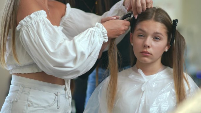 缓慢的运动。特写镜头。女理发师把女孩头上的头发分成几缕，然后用发夹把它们固定在一起。