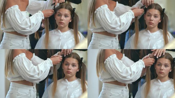 缓慢的运动。特写镜头。女理发师把女孩头上的头发分成几缕，然后用发夹把它们固定在一起。