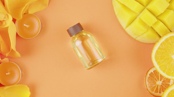 桌子上有一罐化妆品油和香水。柑橘片、鲜花、芒果、香氛蜡烛在橙色背景上的构图特写、俯视图、变焦。夏天明