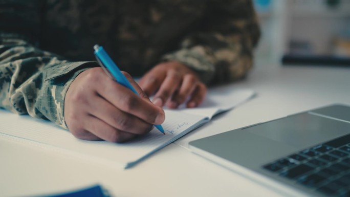 穿着军装的男人在笔记本上写字，用笔记本电脑上网学习，军队