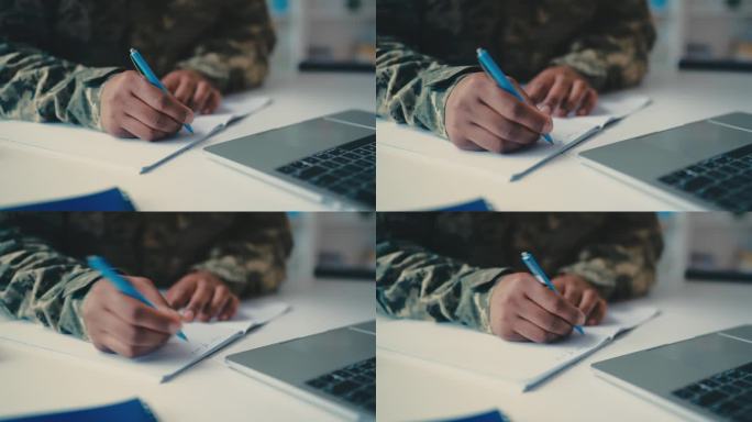 穿着军装的男人在笔记本上写字，用笔记本电脑上网学习，军队