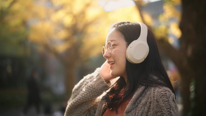 一个亚洲女人在秋天用无线耳机听音乐的特写