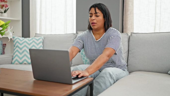 一名西班牙裔女子在明亮的客厅沙发上使用笔记本电脑，沮丧地闭上眼睛，然后仰面躺下。
