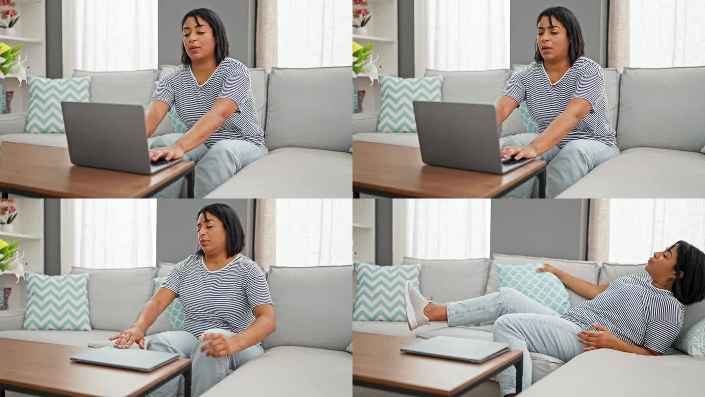 一名西班牙裔女子在明亮的客厅沙发上使用笔记本电脑，沮丧地闭上眼睛，然后仰面躺下。
