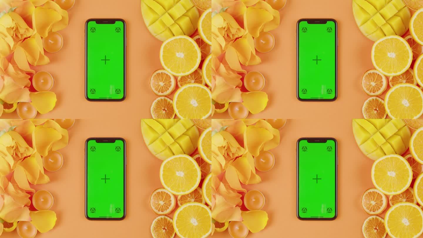 手机与绿色屏幕色度键在橙色背景近距离，顶视图。夏天明亮的纹理工作室拍摄。由鲜花、柑橘片、芒果、香薰蜡