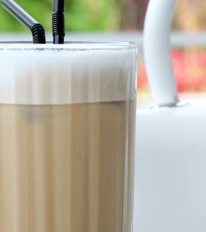 拿铁玛奇朵在美丽的杯子上孤立的白色背景与自然的阴影。卡布奇诺泡沫咖啡和牛奶饮料在一个透明的玻璃杯。印