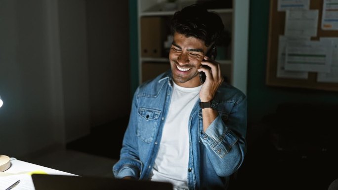 一个微笑的西班牙裔男子在办公室里打电话，穿着休闲的牛仔装。