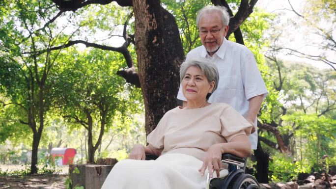 快乐的亚洲老人在公园外为妻子推轮椅，老年夫妇和退休生活的概念