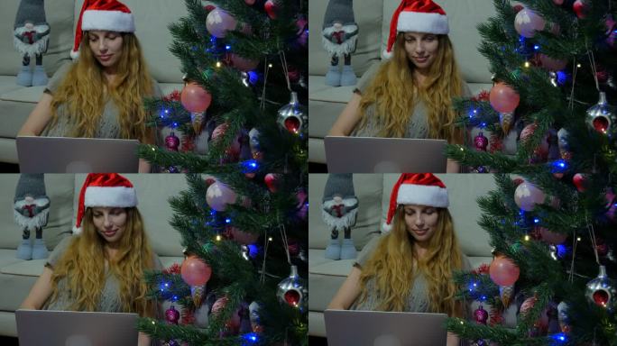 快乐的女人拿着笔记本电脑站在圣诞树旁，圣诞树上装饰着圣诞玩具。