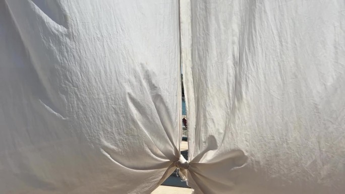 海边晒床上的旧脏白色破薄纱窗帘，海边度假时的风帆窗帘