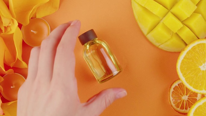 桌子上有一罐化妆品油和香水。柑橘片、鲜花、芒果、香氛蜡烛在橙色背景上的构图特写、俯视图、变焦。夏天明