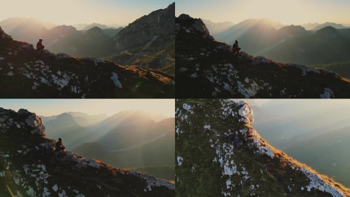 空中无人机拍摄的山地自行车手在阳光明媚的日子里坐在巨大的悬崖边使用智能手机的画面