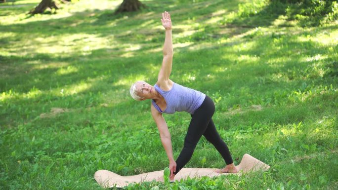 中年妇女在户外做伸展三角体式瑜伽。