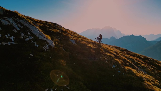 在阳光明媚的日子里，骑自行车的人在大山上移动的高角度无人机拍摄