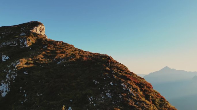 在阳光明媚的日子里，山地自行车手在巨大的岩石悬崖上骑自行车的无人机镜头