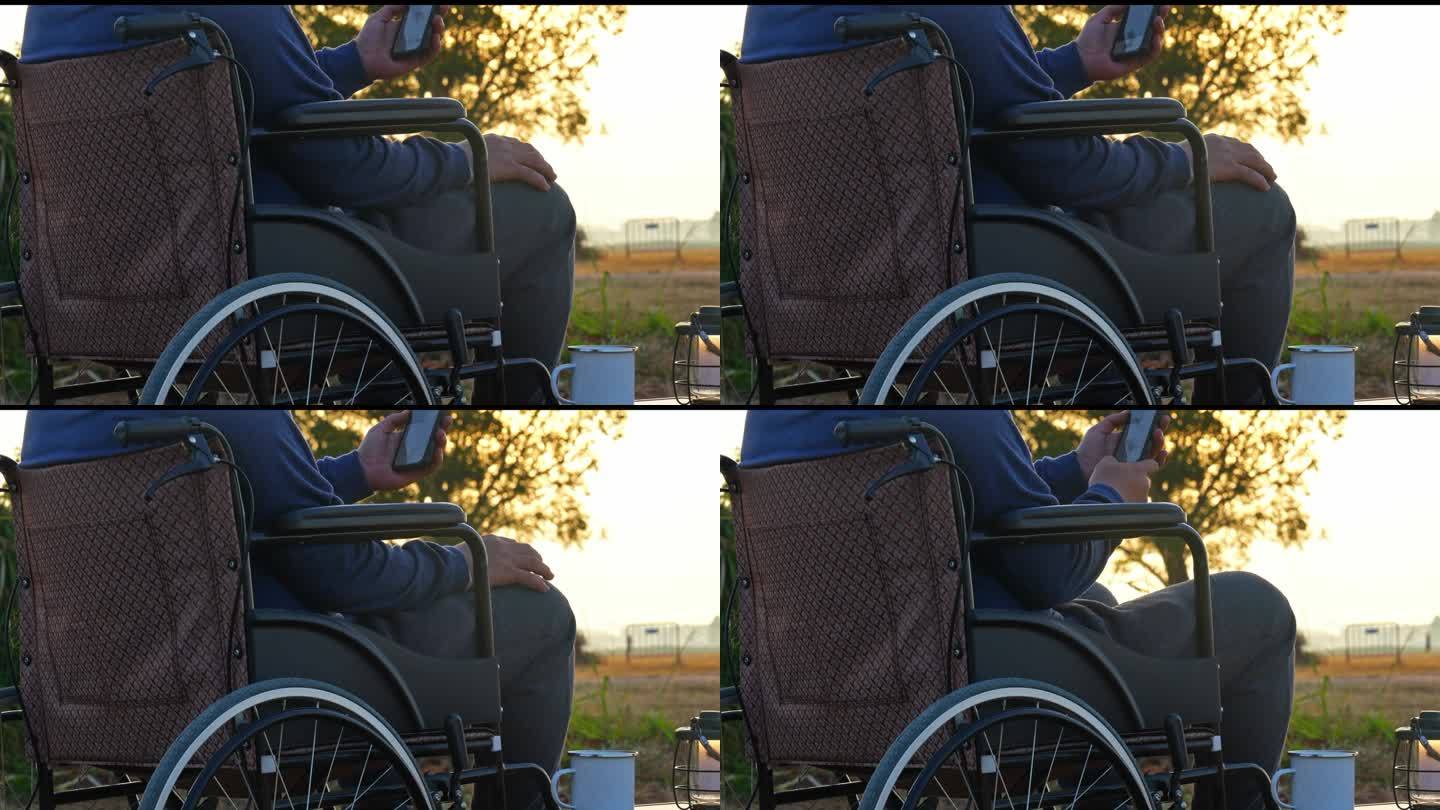 一个人坐在轮椅上，拿着智能手机，看着第一个金色的日出。